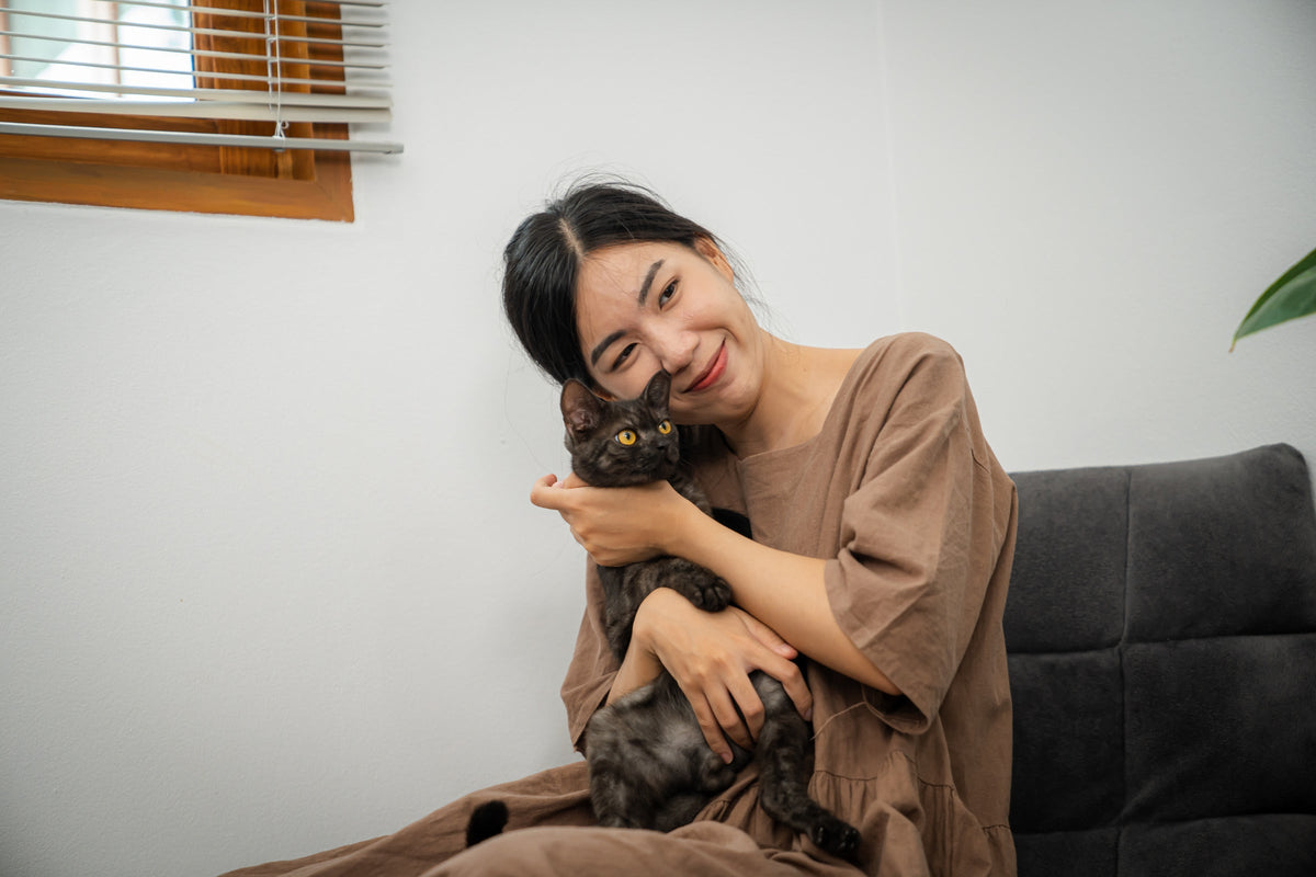 A person cuddling a dark-coated cat on a sofa.