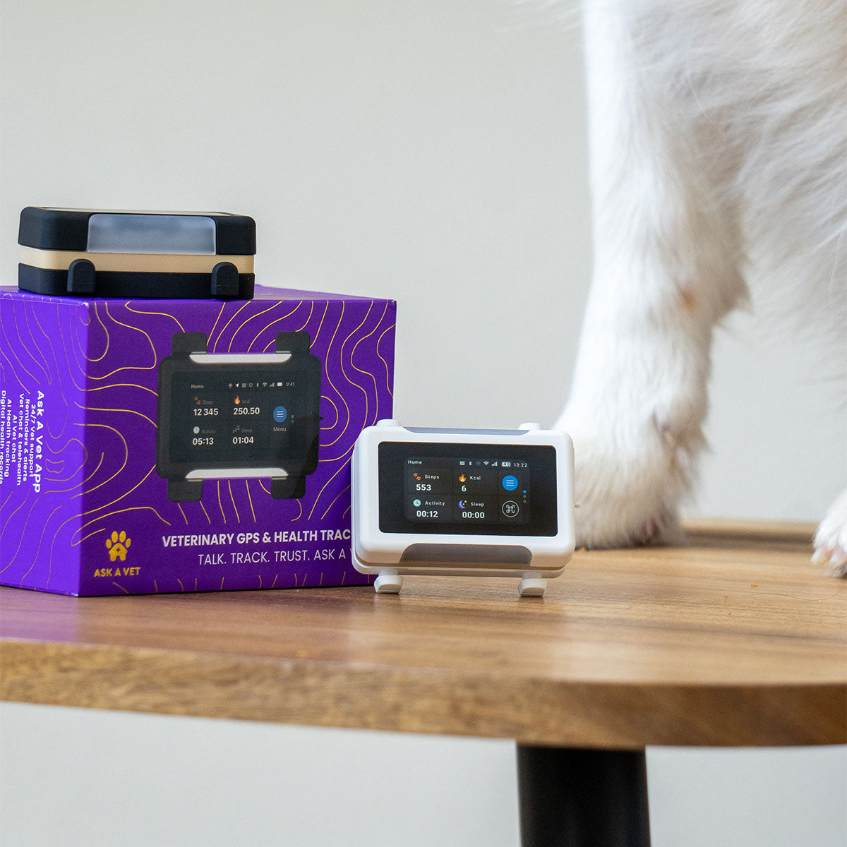 White / Gold | Smart GPS & Health Tracker: The White / Gold tracker beside its purple box, with a dog behind the table